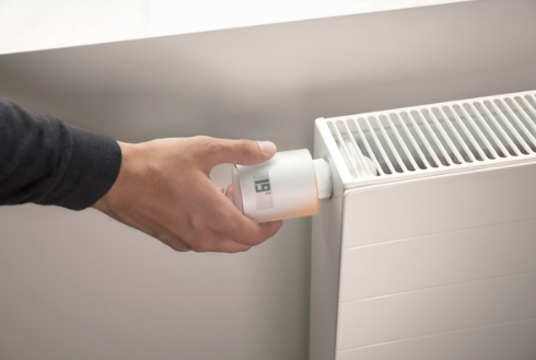 Main qui règle la température de la pièce avec une tête thermostatique connectée